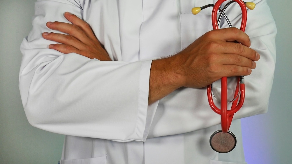 A healthcare professional in a white coat with arms crossed, holding a red stethoscope.